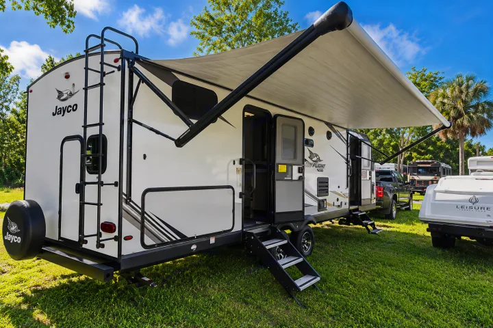 A white Jayco travel trailer rv rental is parked on grass with its awning extended and steps down, ready for use.. Jayco White Hawk 2022