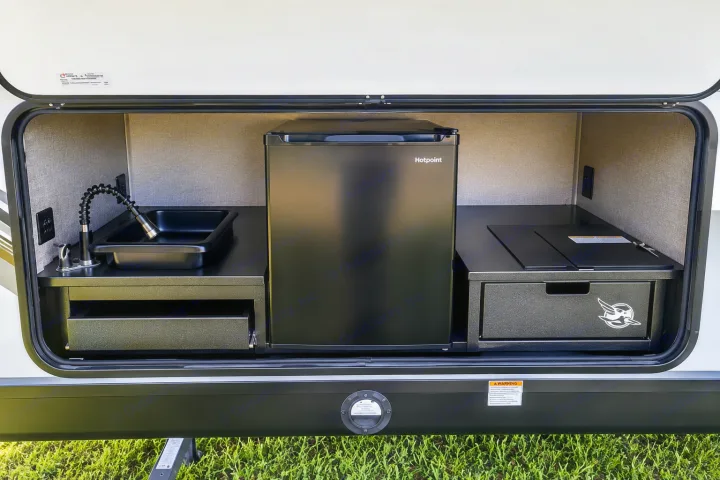 RV rental outdoor kitchen featuring a sink with a flexible faucet, a Hotpoint mini-fridge, and a pull-out grill.. Jayco White Hawk 2022