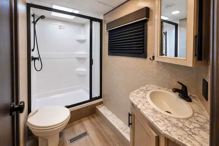 Inside an RV rental bathroom: a clean shower stall, toilet, and vanity with a sink & mirror. Compact, modern, & functional.. Jayco White Hawk 2022