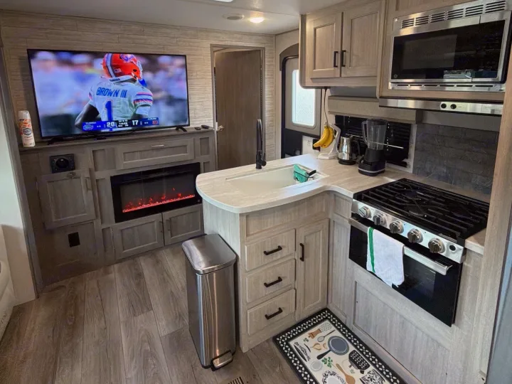 This RV rental features a living area with a TV (football game visible), electric fireplace, and a well-equipped kitchen.. Coachmen Catalina Legacy 2024