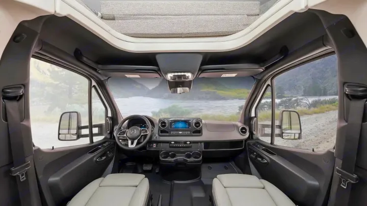 This rv rental camper van's spacious cockpit features a modern dashboard, comfortable seats, and an inviting scenic view.. Winnebago Navion 2023