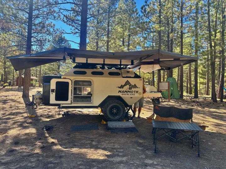 This Mammoth Overland camper trailer, an ideal rv rental, is set up with an awning in a sun-dappled forest campsite.. Mammoth Overland HV 2022