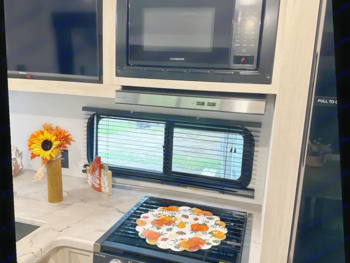 Inside an RV rental kitchen: a microwave, stove, TV, and window with fall decor like a sunflower vase and pumpkin placemat.. Forest River Palomino Puma Camping Edition 2025