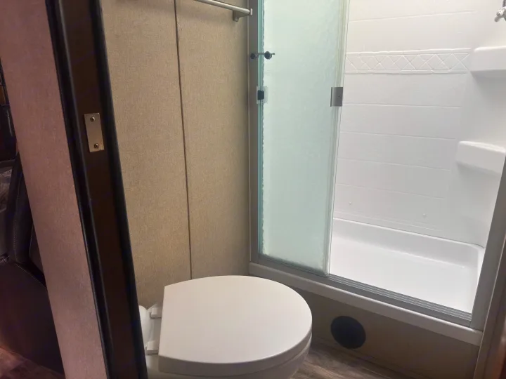 Compact RV rental bathroom: white toilet, shower with frosted sliding glass door, and textured walls.. Grand Design Reflection 2019