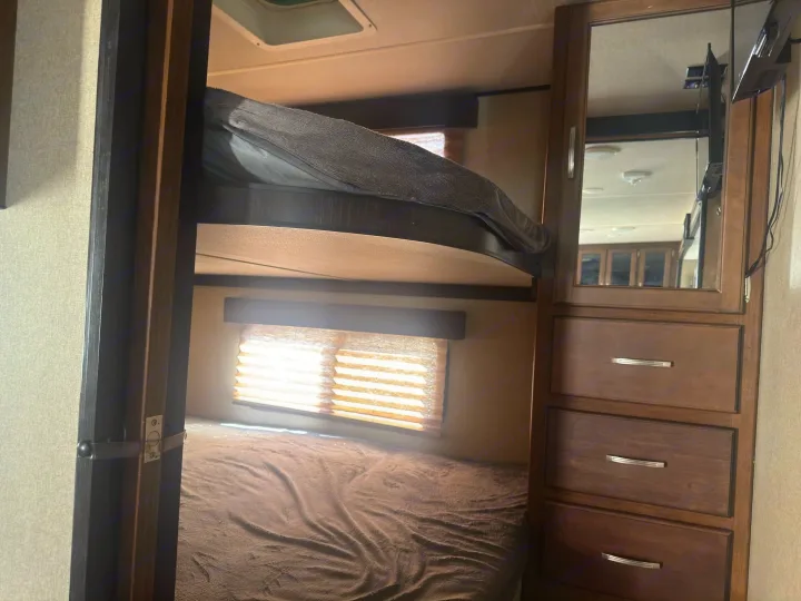 This RV rental features cozy bunk beds, a sunlit window with blinds, and a mirrored dresser, offering practical space for travel.. Grand Design Reflection 2019