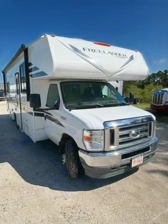 White Freelander Class C RV rental, a compact motorhome ready for travel, parked on a sunny gravel lot.. Coachmen Freelander Freelander 2022