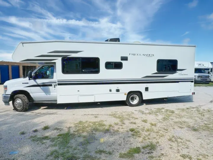 A white Freelander Class C motorhome rv rental with black decals, parked on gravel under a blue sky.. Coachmen Freelander Freelander 2022