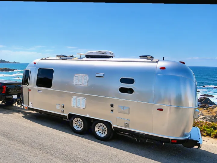 A silver Airstream travel trailer, ideal for an RV rental, sits parked against a stunning blue ocean backdrop.. Airstream International 2017