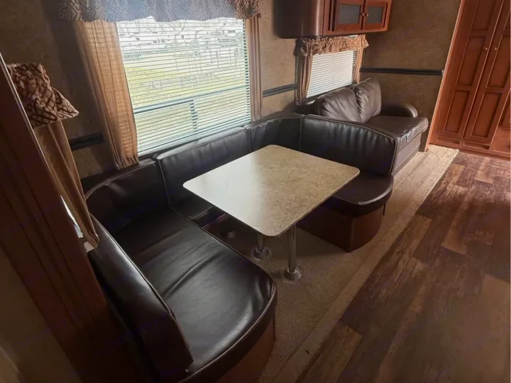 Cozy RV rental interior featuring a U-shaped dinette with a light table and brown leather-like seating, plus a sofa.. Aspen Trail Aspen Trail Trailer 2014