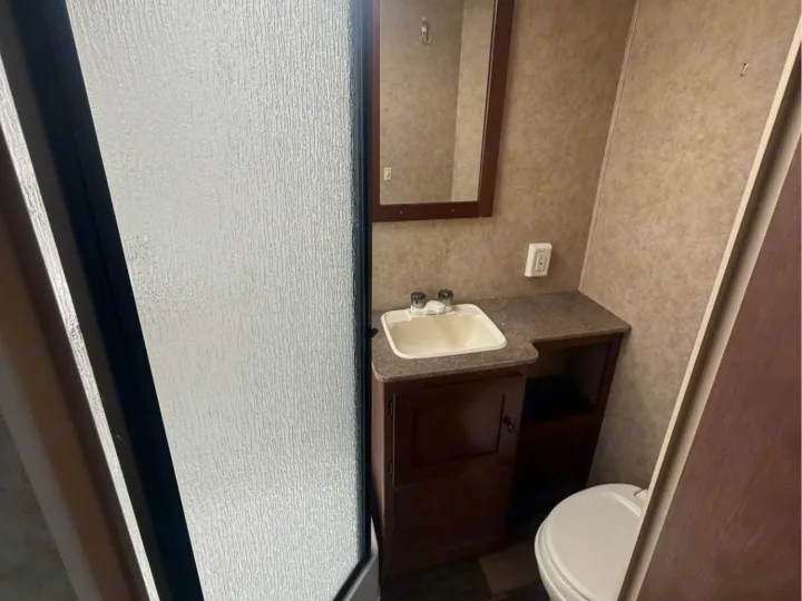 Inside your RV rental: a clean, compact bathroom with sink, toilet, mirror, and a frosted glass shower door.. Aspen Trail Aspen Trail Trailer 2014