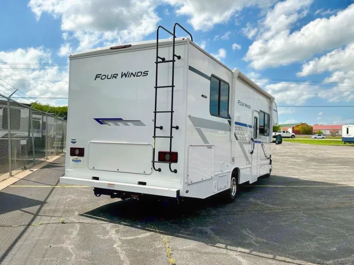 White Four Winds motorhome RV rental, featuring a rear ladder & sleek side profile, parked on asphalt under a blue sky.. Four Winds 28Z 2026