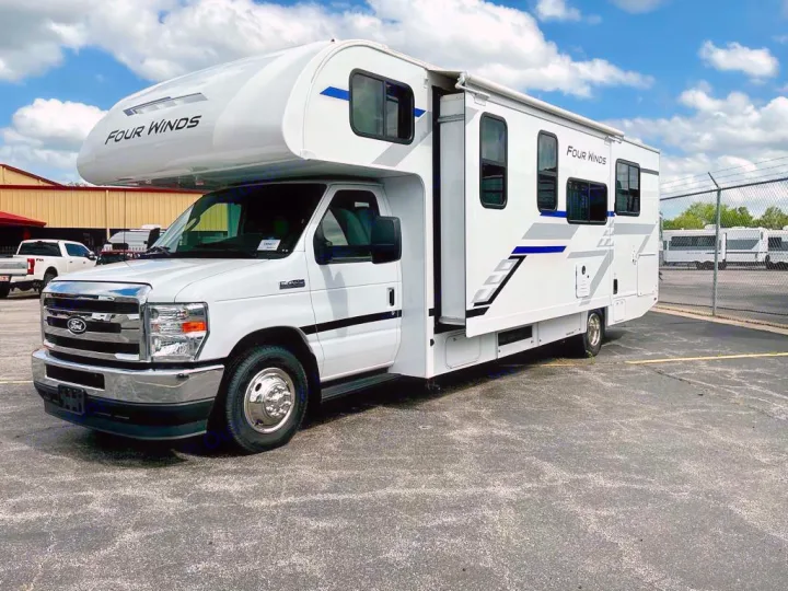 White Four Winds Class C RV, featuring blue/grey accents, available for rv rental. Parked outdoors under a blue sky.. Four Winds 28Z 2026
