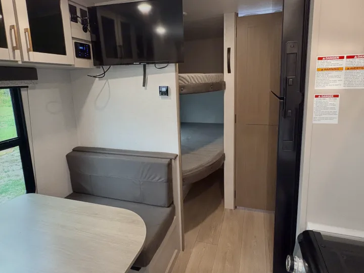 Inside an RV rental, this cozy living space features a dinette, TV, and bunk beds, perfect for family travel.. Jayco Jay Flight 2027