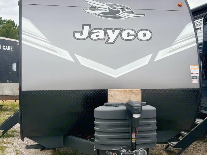 Front of a gray Jayco RV rental travel trailer, showcasing propane tanks and an electric tongue jack for easy setup.. Jayco Jay Flight 2027