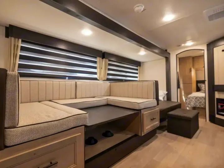 This modern RV rental features a cozy U-shaped dinette with light cushions and dark wood accents. A bedroom is visible in the background.. Forest River Cherokee Grey Wolf 2026
