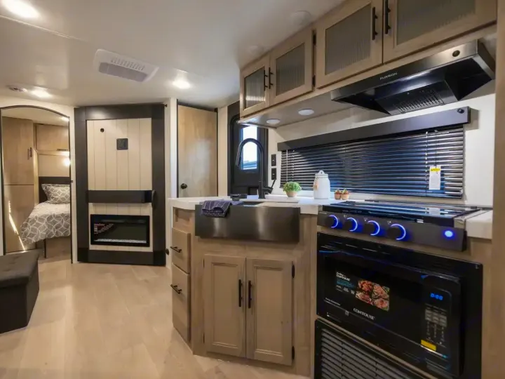 Modern rv rental interior showcasing a kitchen with stove, microwave, and sink, plus a peek into the bedroom.. Forest River Cherokee Grey Wolf 2026