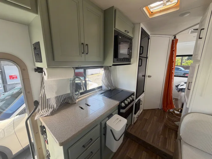 RV rental interior: kitchen with green cabinets, sink, stovetop, microwave, and fridge. Cozy camper living space.. Thor Quantum 2018