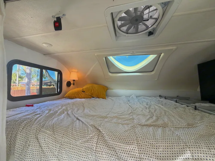 This RV rental's bedroom features a patterned bed, yellow pillows, window view, ceiling fan, skylight, and wall lamp.. Thor Quantum 2018
