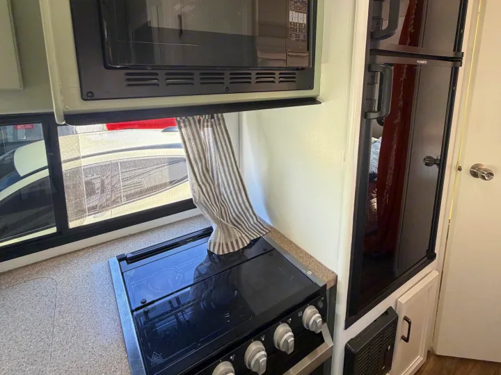 Compact RV rental kitchen featuring a microwave, stove, and Dometic refrigerator, ideal for travel.. Thor Quantum 2018