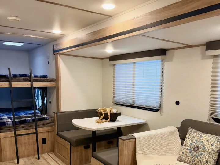 This cozy RV rental interior features comfortable bunk beds, a dinette, and sofa for a functional living space.. Gulf Stream Enlighten SE 2025
