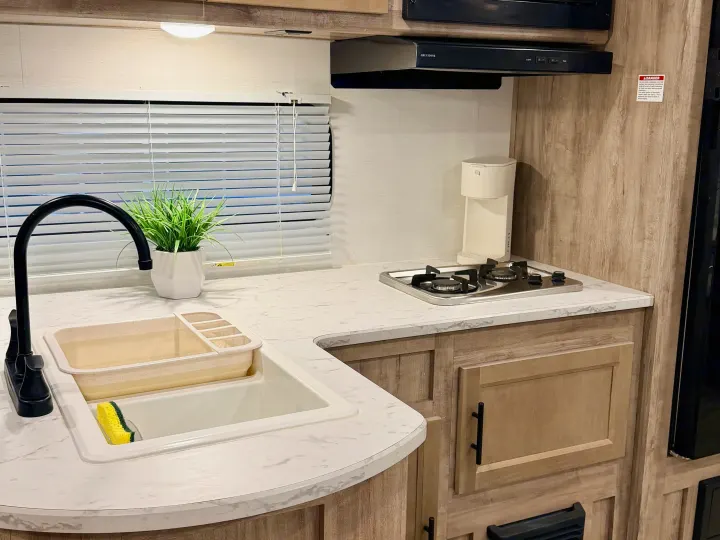 This clean, modern RV rental kitchen features a sink, 2-burner stove, coffee maker, and ample counter space for travel.. Gulf Stream Enlighten SE 2025