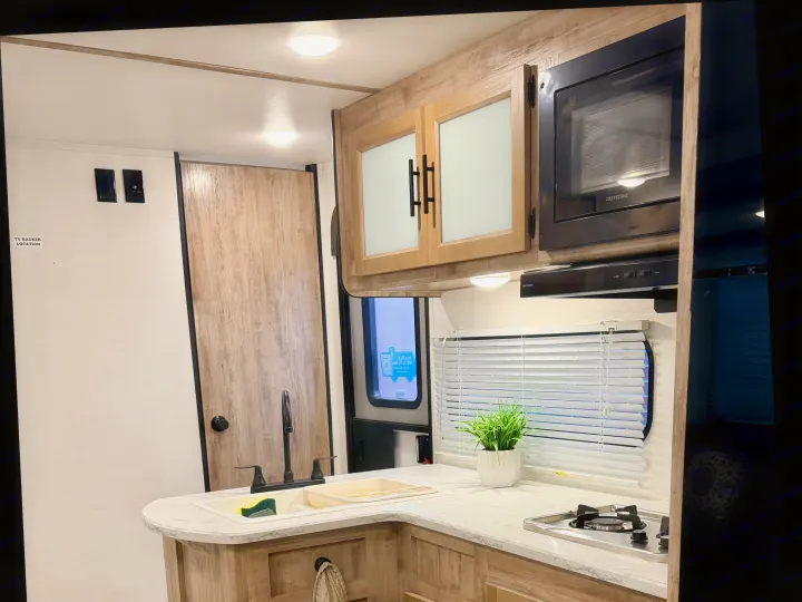 Modern RV rental kitchen featuring a microwave, sink, stove, and light wood cabinets for comfortable travel.. Gulf Stream Enlighten SE 2025
