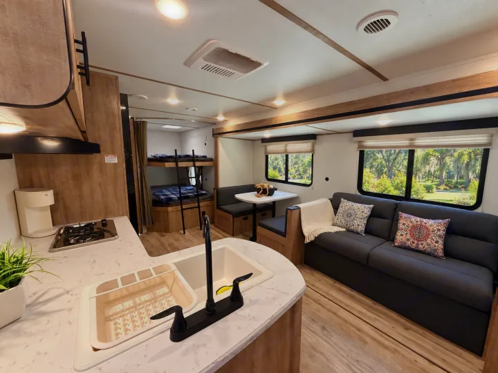 Spacious RV rental interior featuring a full kitchen, dining area, comfy sofa, and bunk beds. Enjoy the view through large windows.. Gulf Stream Enlighten SE 2025