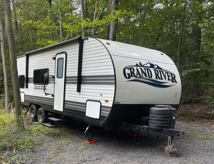 White Grand River rv rental trailer parked in a wooded campsite, ready for an outdoor adventure.. Forest River grand river 2024