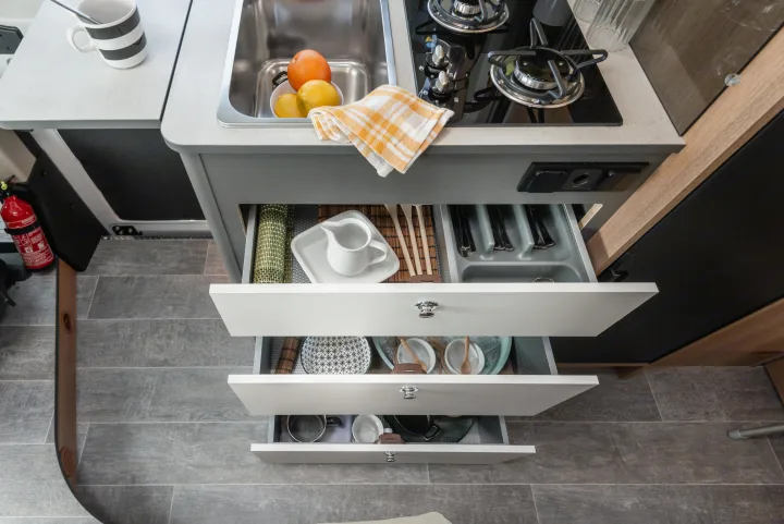 This compact RV rental kitchen showcases a sink, stovetop, and neatly organized drawers filled with dishes and cutlery.. Giottiline 60 Be Young 2027