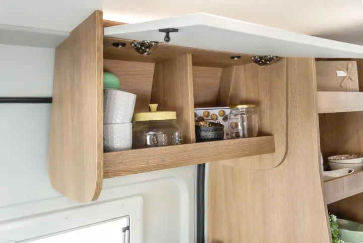 Organized overhead kitchen cabinet in an RV rental, showing mugs, jars, and bowls within its compact storage.. Giottiline 60 Be Young 2027