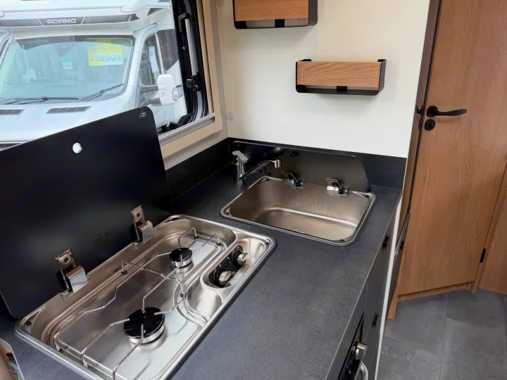 Inside this RV rental: a compact kitchen with a two-burner gas hob, sink, and dark gray countertop for efficient travel cooking.. JOA 60F 2027