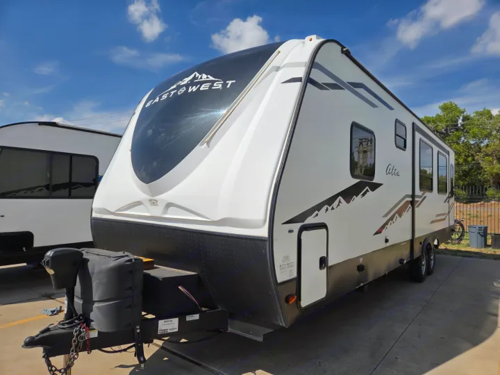 This white and black East to West Alta travel trailer rv rental is parked outdoors under a blue sky, ready for adventure.. Alta 2850KRL 2021