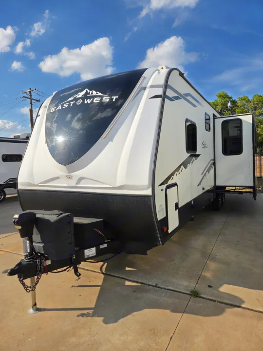 A white EastWest Alta travel trailer RV with black accents and an open door, ideal for your next rv rental adventure.. Alta 2850KRL 2021
