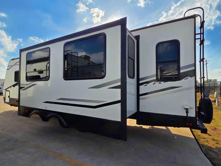 Side view of a white and black RV rental with extended slide-outs, spare tire & ladder. Perfect for your road trip adventure.. Alta 2850KRL 2021