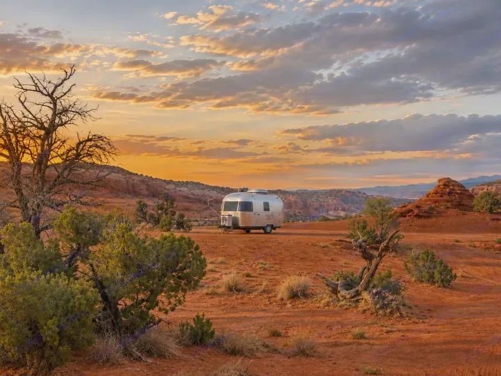 An Airstream RV rental gleams in a vast, red desert landscape at sunset, surrounded by sparse brush and distant mountains.. Airstream Bambi 2022