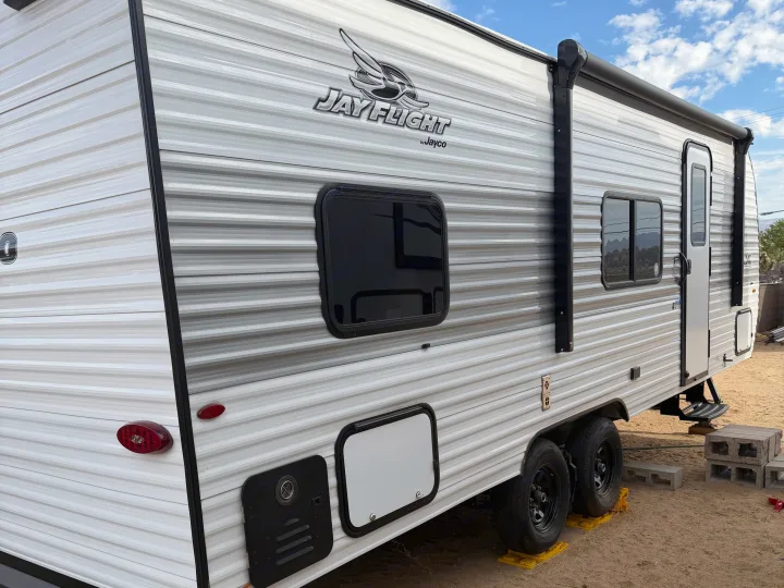 Side view of a white/grey Jayco Jay Flight rv rental, a travel trailer with striped siding, tinted windows, and an awning.. Jayco Jay Flight SLX Sport Edition 2026