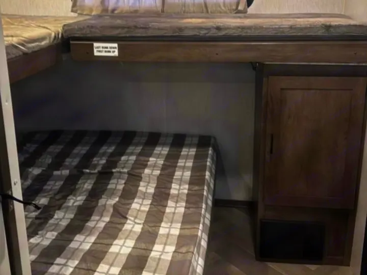 RV rental bunk beds. Lower bed with plaid comforter, upper bunk above, and a dark wood storage cabinet on the right.. Forest River Salem 2022