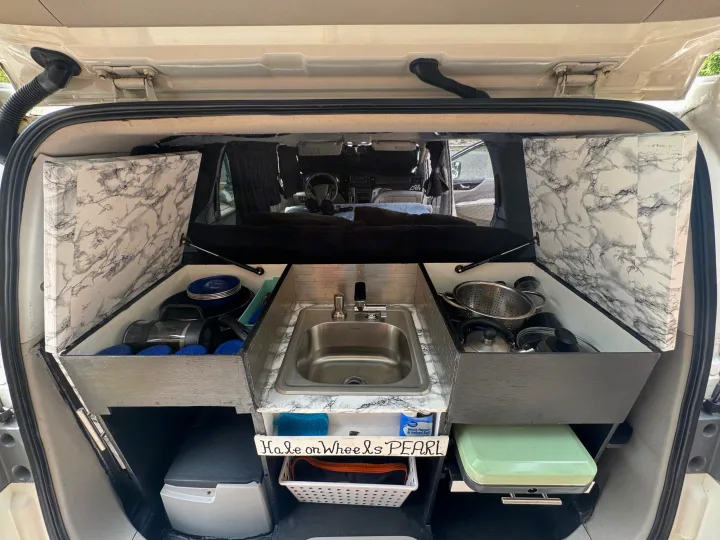 RV rental van's custom kitchen boasts a sink, stove, and marbled storage. Perfect for compact camping adventures!. Nissan Quest 2017