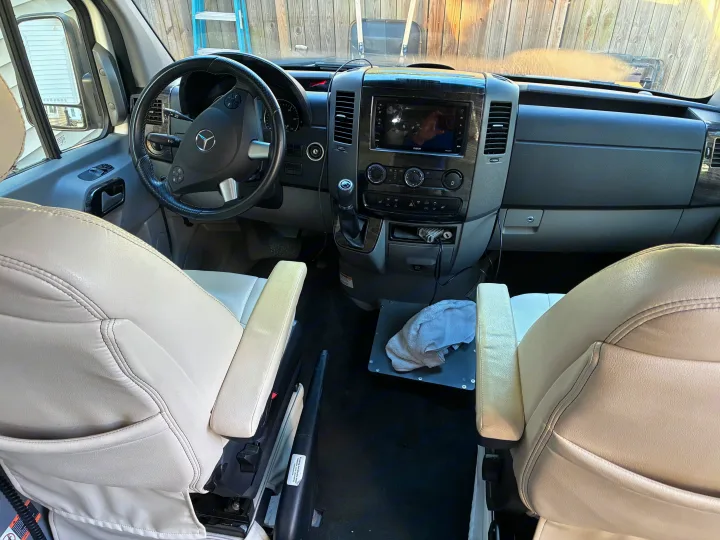 Explore the modern front cabin of this rv rental, featuring a Mercedes steering wheel, dashboard with infotainment, and comfortable light seats.. Airstream Interstate 2021