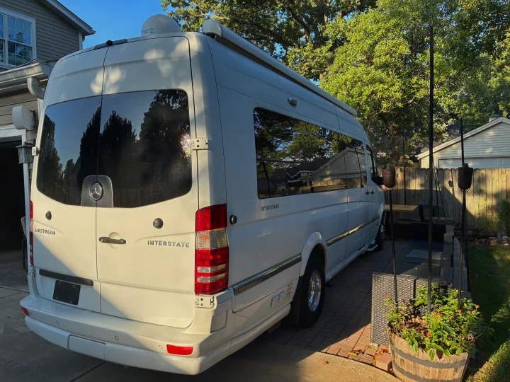 A white Airstream Interstate RV rental, a premium camper van, parked at home. Features roof satellite & awning.. Airstream Interstate 2021