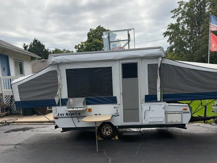 Expanded white/gray Jayco pop-up camper, an ideal rv rental option, is set up on a driveway with an outdoor stove and table.. Jayco Jay 2009