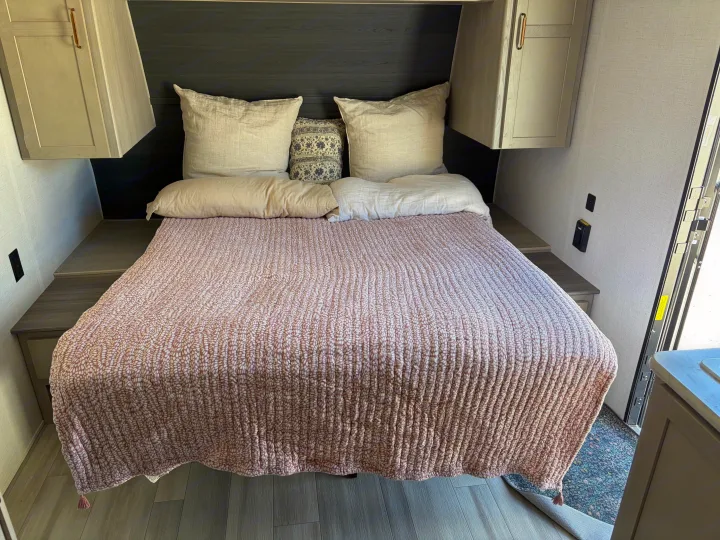 Inviting RV rental bedroom with a comfy bed, neutral pillows, a pink patterned quilt, and convenient overhead cabinets.. Keystone RV Springdale 2024