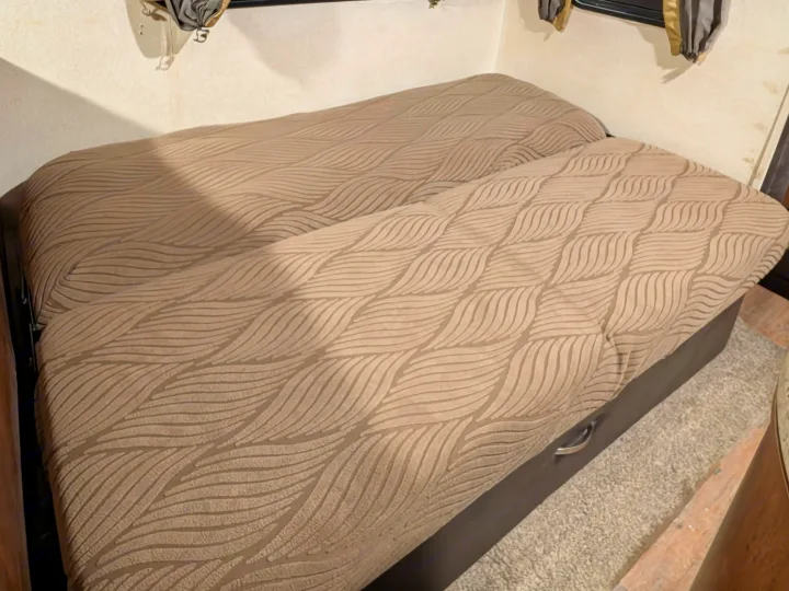 Cozy RV rental sleeping area features textured wavy bedding, window coverings, and under-bed storage for comfortable travel.. Forest River Salem 2017