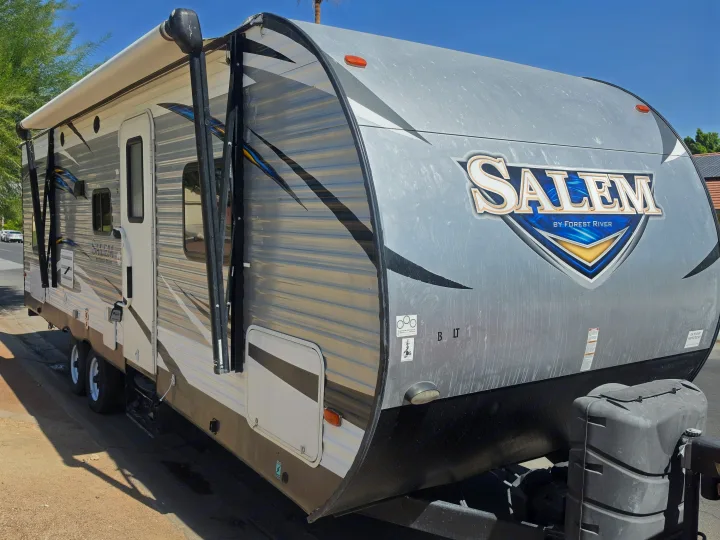A grey Salem Forest River travel trailer RV rental, with its awning extended, parked outdoors on a sunny day.. Forest River Salem 2017
