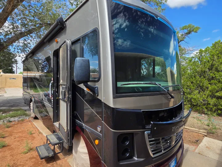 Front view of a two-tone motorhome, possibly an rv rental, parked outside with its entry steps deployed near trees.. Holiday Rambler Vacationer 2019