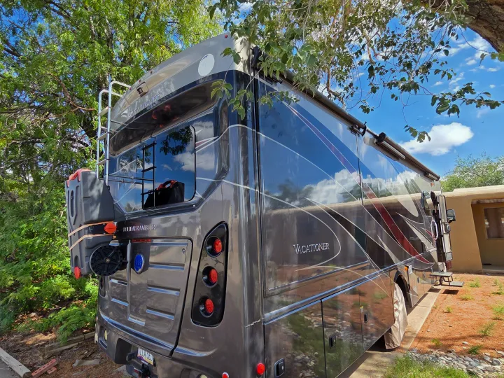 "Vacationer" RV rental motorhome, dark gray and sleek, parked outside reflecting the blue sky and trees.. Holiday Rambler Vacationer 2019