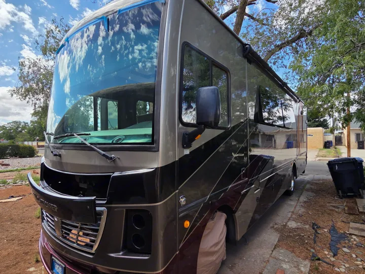 A large, two-tone RV, possibly an rv rental, with its front panel open. A cloudy sky and trees reflect on its windshield.. Holiday Rambler Vacationer 2019