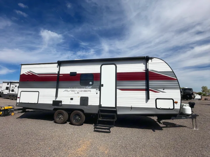 Prime Time Avenger travel trailer RV rental with distinctive white, red, and grey stripes, parked on a gravel lot.. Avenger Avenger Trailer 2026