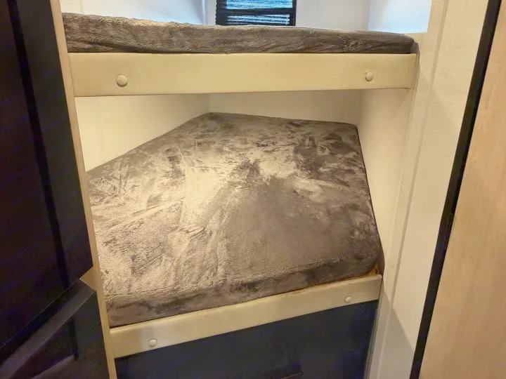Compact bunk beds in an RV rental, featuring grey textured bedding on both upper and lower bunks, offering a cozy sleeping space.. Avenger Avenger Trailer 2026