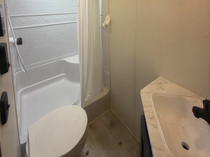 Compact RV rental bathroom features a white shower/tub, toilet, and sink with light walls and wood-look floor.. Avenger Avenger Trailer 2026